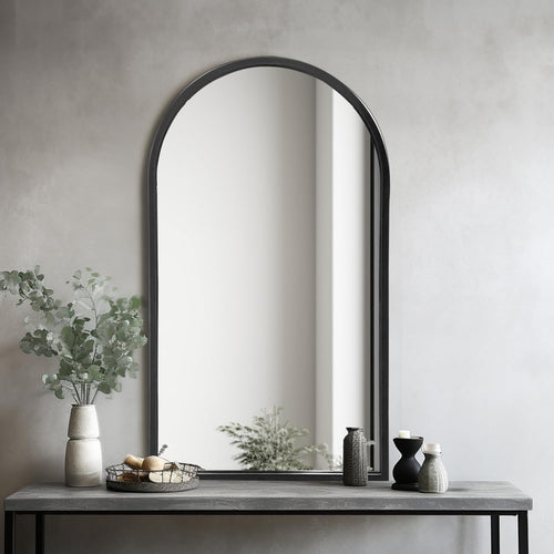 Arched iron mirror on a gray console table with decorative items against a neutral wall.
