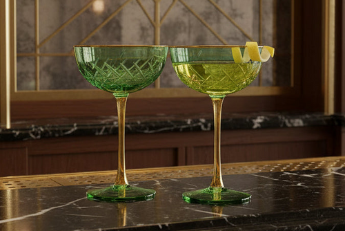 Art Deco Coupe Cocktail glasses in green with lemon slices on a marble surface.