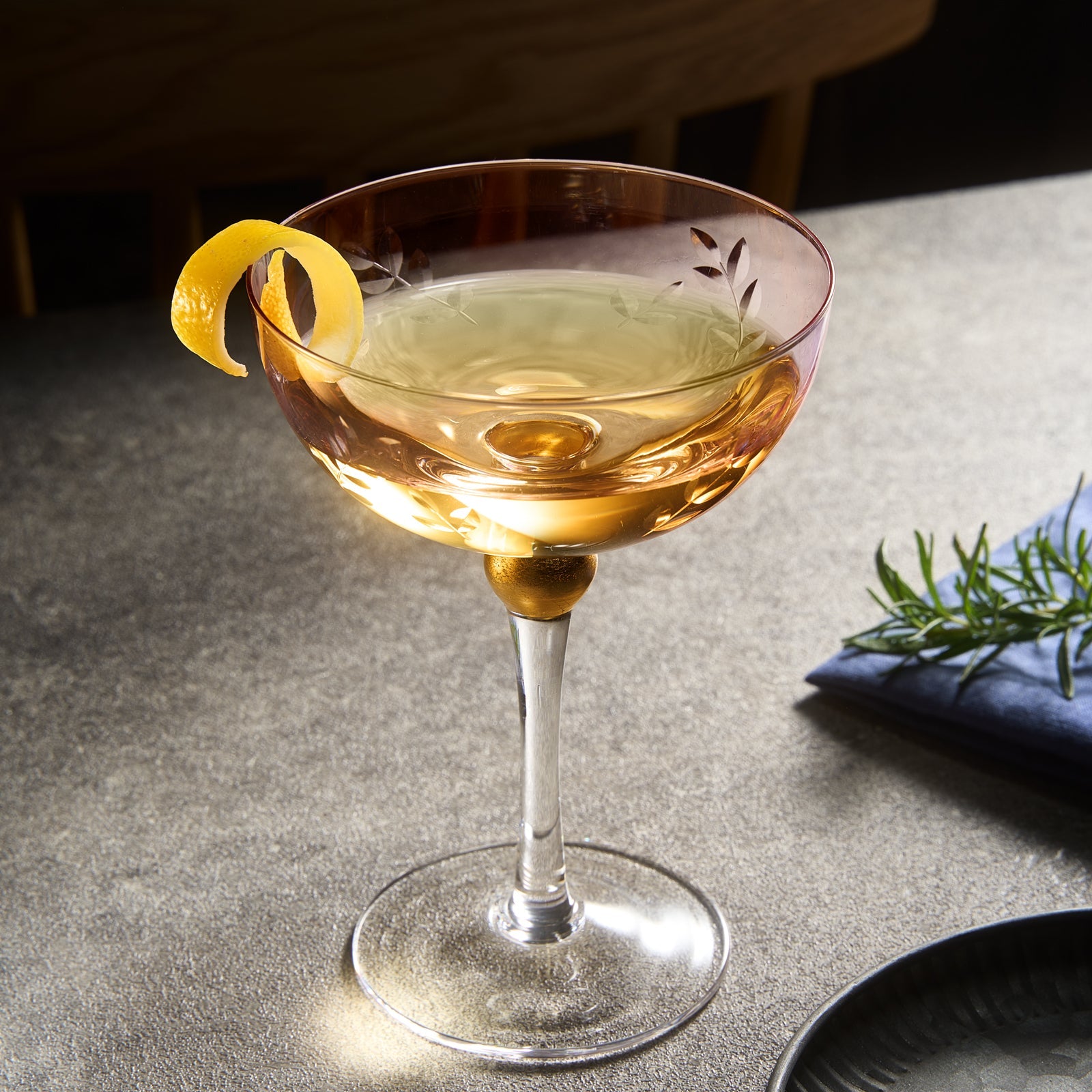 Art deco coupe cocktail glass with a lemon twist on a textured surface