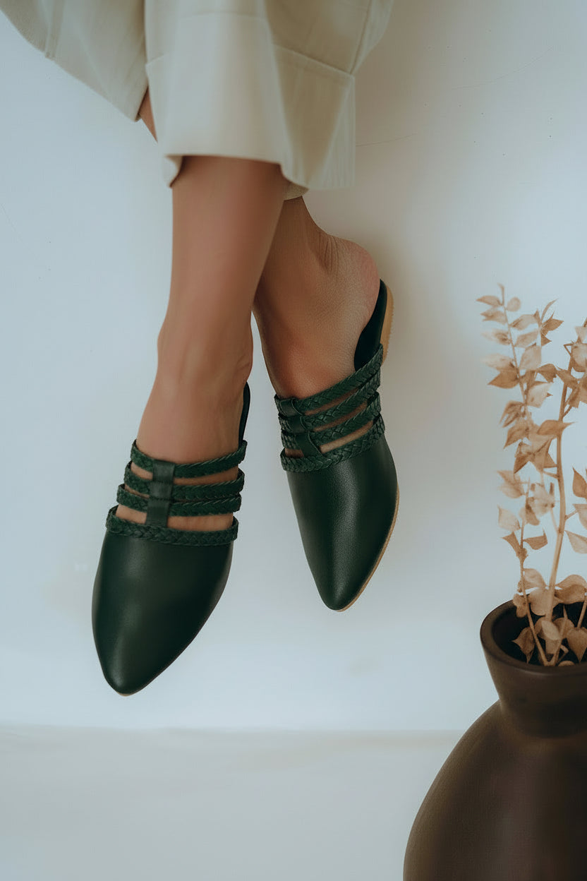 Audrea pointed toe loafers in emerald with braided details, on model next to a vase with dried plants on a white background