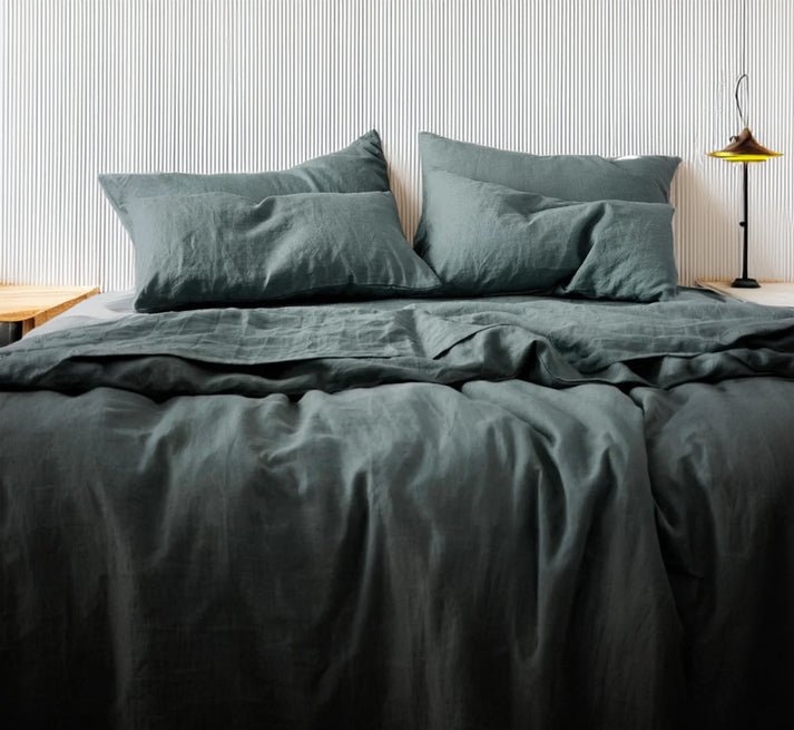 Deep sea green linen and cotton duvet set on a bed with striped wallpaper in the background