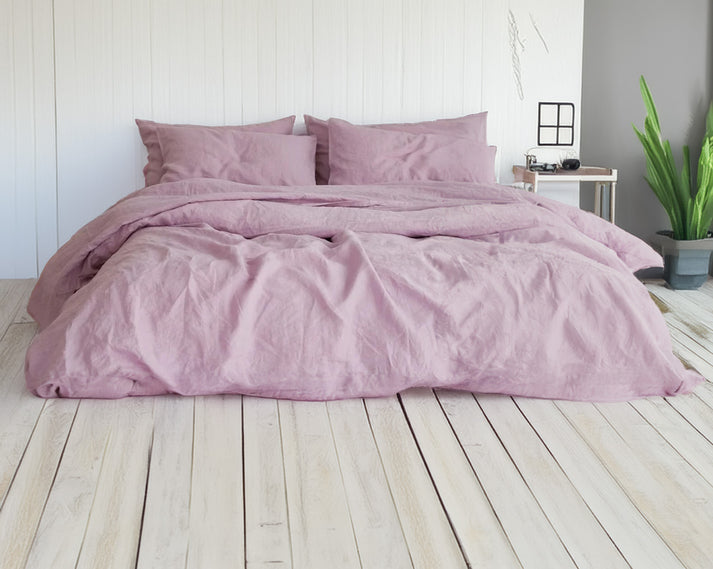 Lilac linen and cotton duvet set on a bed in a room with a plant and small table.
