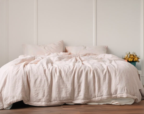 Linen and cotton duvet cover and shams in light pink in a room with light-colored walls.