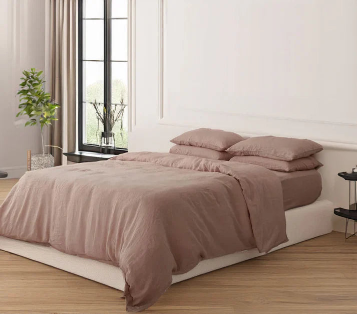 Bed with clay color linen and cotton duvet set in a bright bedroom with large windows.
