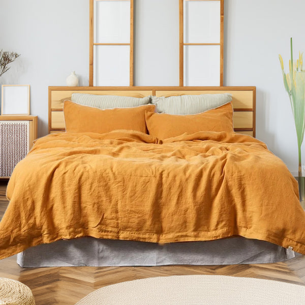 Bed with mustard yellow linen and cotton duvet set and wooden headboard in a room with white walls and wooden floor.