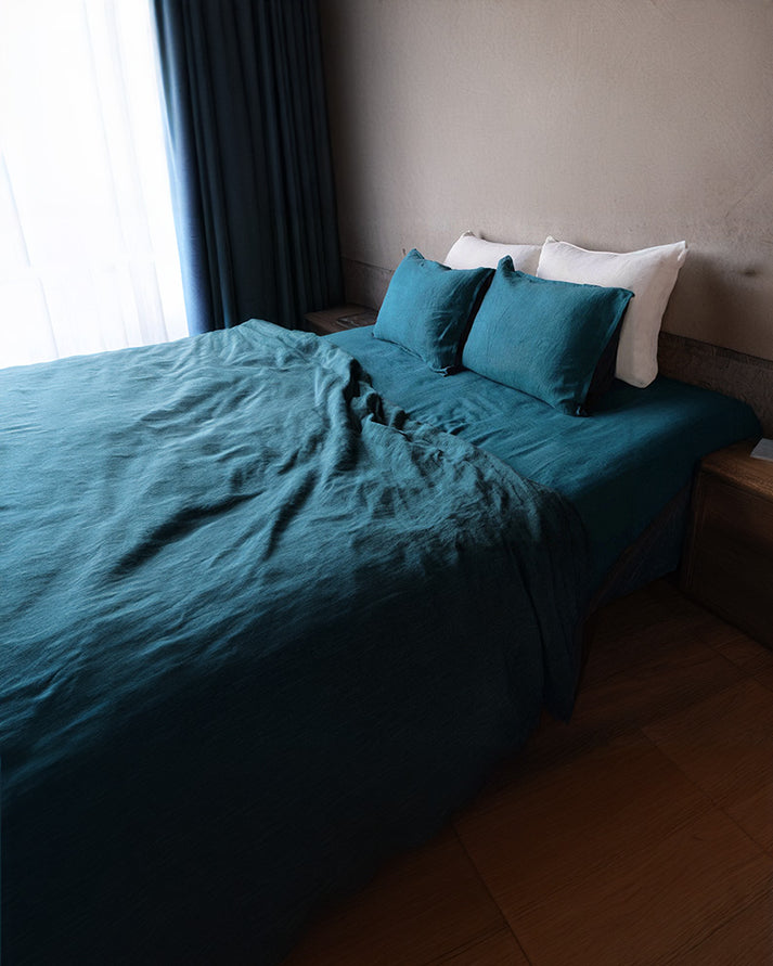 Bed with  peacock blue and cotton duvet cover and shams in a dimly lit room