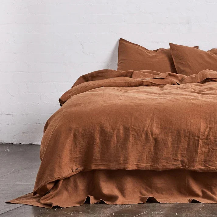 Rust linen and cotton duvet set on a bed against a white brick wall.