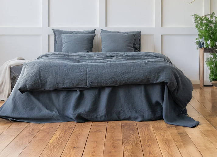Midnight blue linen and cotton duvet set on a bed in a room with wooden flooring and a plant.