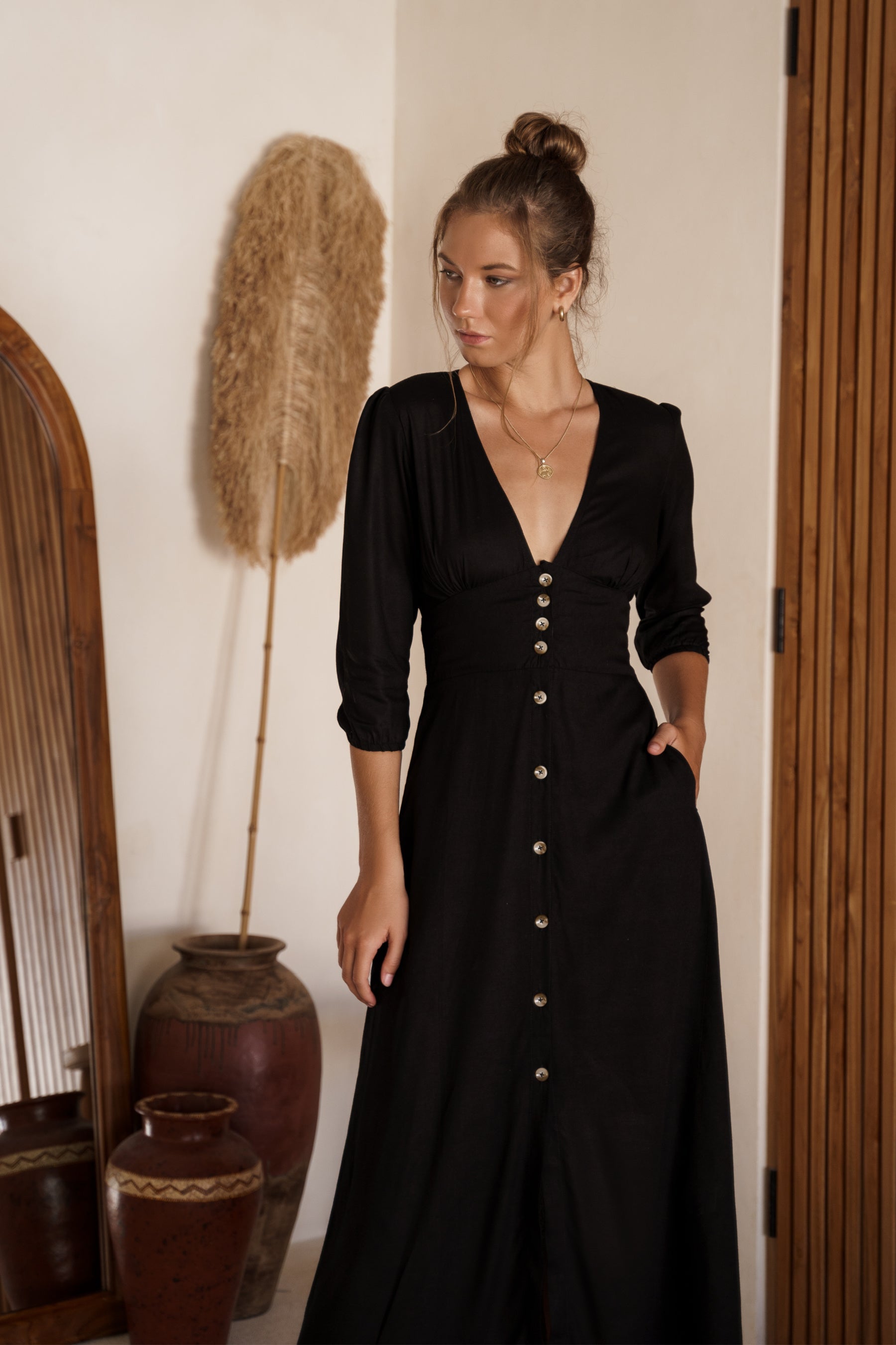 Woman wearing Sofia black dress with buttons in a room with decorative elements.