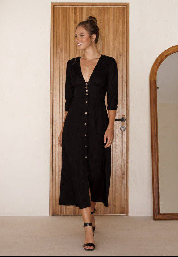 Woman wearing a black dress with buttons standing in front of a wooden door.